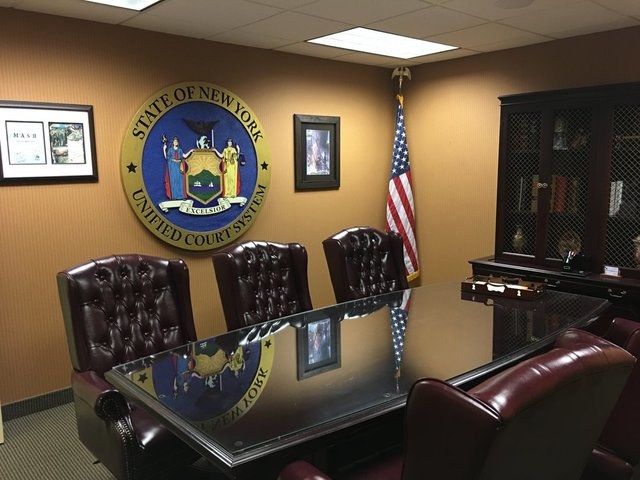 The firm&rsquo;s conference room, with the seal of the New York State Unified
                    Court System on the wall